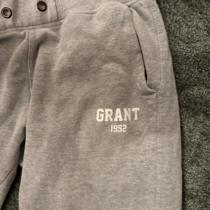 Grå mjukisbyxor från Grant 1952 - Säljer ett par grå mjukisbyxor från Grant i storlek M. Byxorna har en bekväm passform med resår i midjan och muddar vid bensluten. Perfekta för en avslappnad dag hemma eller en promenad i parken. De har också praktiska fickor och en snygg logga på sidan. 🩶