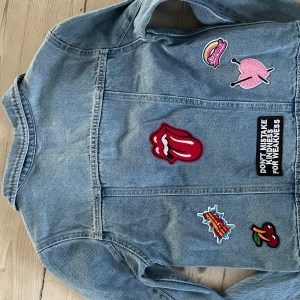 Jeansjacka med patches från Levi's - Säljer en helt ny snygg jeansjacka från Levi's i storlek 152-158. Den har flera färgglada patches, som ger en unik look. 