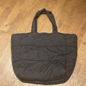 Svart quiltad väska - Säljer en stor och rymlig svart väska i quiltat material. Perfekt för vardagsbruk eller när du behöver extra utrymme. Väskan har medellånga handtag och en praktisk innerficka med dragkedja för säker förvaring av småsaker. Den är i mycket bra skick och redo för nya äventyr!