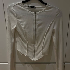 Ribbad tröja med dragkedja  - Finns i tre färger: vit, svart och brun. Tröjan har en tight passform och långa ärmar. Säljs styck pris!