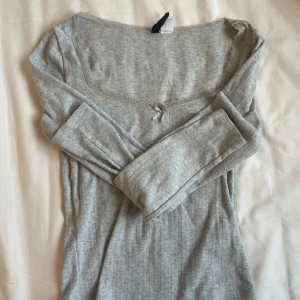 Grå långärmad topp från H&M Divided - Säljer denna super gulliga gråa långärmade topp från H&M Divided. Den har en söt spetskant och en liten rosett vid halsringningen. Perfekt för både vardag och fest! 😍💓💓