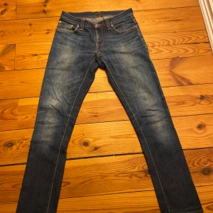 Nudie Jeans med slitning - Säljer ett par snygga blå jeans från Nudie Jeans i bra skick 9/10✅                                                                    De har en klassisk femficksdesign och slitna detaljer för en cool look. Perfekta för både vardag och fest! Passar bra till sneakers eller kängor. Storlek: 27/32✅