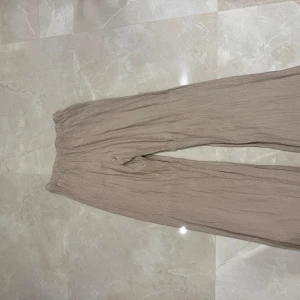 Beige byxor från Zara - Säljer ett par superbekväma beige byxor från Zara i storlek S. De har en loose fit och är gjorda i ett lätt och luftigt material, perfekt för varma dagar. Byxorna har en elastisk midja för extra komfort. Perfekta för en avslappnad stil!
