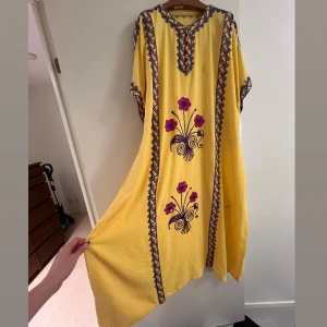 Gul maxiklänning  - En gul klänning med broderade blommor och detaljer i olika färger.   Klänningen har en rund halsringning och korta ärmar.   Den är löst sittande och har en rak silhuett.  Passar small, medium, large. 135 cm hals till ankel.