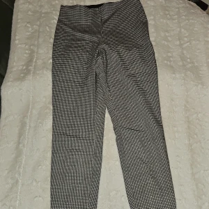 Rutiga ankelbyxor nytt - Nya Snygga svarta ankelbyxor med vitt rutmönster. Byxorna har en smal passform och är tillverkade i ett stretchigt material. De har en dragkedja och knapp i sidan och även resår . En liten slits nedtill