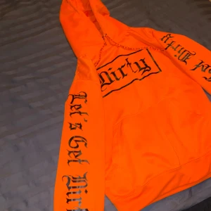 Orange hoodie med tryck - Säljer en cool orange hoodie med texten 'Dirty' och 'Let's Get Dirty' i svart tryck. Perfekt för att sticka ut i mängden! Den har en klassisk känguruficka och en bekväm huva med dragsko. Grym för både vardag och fest! 🧡