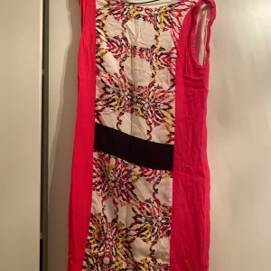 Färgglad ärmlös klänning - Säljer en superfin ärmlös klänning med ett färgglatt blommönster i rosa, svart och gult. Klänningen har en svart midjedetalj som ger en snygg siluett. Perfekt för sommarens fester eller en dag på stan. Materialet känns lätt och bekvämt. Passa på att köpa denna unika klänning!