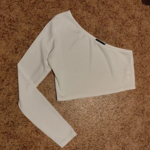 Vit oneshoulder topp från Boohoo - Säljer en stilren vit oneshoulder topp från Boohoo. Den har en lång ärm och är gjord i ett ribbat material som ger en snygg textur. Perfekt för en utekväll eller fest! 🕺