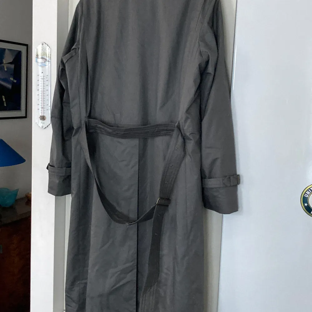 Säljer en elegant grå trenchcoat från Dress Bocaj of Sweden. Den har en klassisk design med bälte i midjan och långa ärmar. Perfekt för höst och vår. Jackan är i mycket bra skick och gjord av bomull, vilket gör den både bekväm och stilren.. Takit.