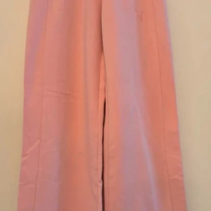 Rosa mjukisbyxor från Puma - Superbekväma, trendiga rosa mjukisbyxor från Puma i storlek 10-12 år. Perfekta för en chill dag hemma eller en avslappnad promenad. Byxorna har en elastisk midja och en praktisk bakficka. Materialet är en mjuk blandning av bomull och polyester.