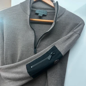 Brun tröja med dragkedja från Snoot - Snygg brun tröja från Snoot med halv dragkedja och cool detalj på ärmen. Perfekt för höst och vinter, den är både stilren och bekväm. Passar bra till både vardag och lite finare tillfällen.  Den har krympt i storlek så sitter som en s 🧥