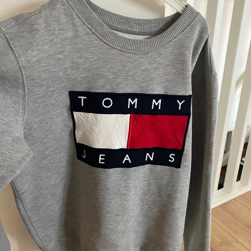 Säljer en snygg grå sweatshirt från Tommy Hilfiger i mycket bra skick. Den har ett stort, ikoniskt logotyptryck i rött, vitt och blått på framsidan. Perfekt för en casual look och passar bra till både jeans och joggers. Superbekväm och stilren! . Tröjor & Koftor.