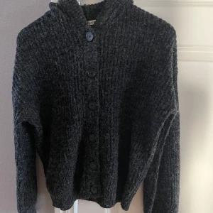 Grå kofta från NA-KD - Säljer en supermysig grå kofta från NA-KD i storlek XS. Den är stickad och har knappar hela vägen ner samt en skön huva!❤️‍🔥
