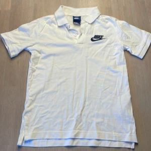 Vit pikétröja från Nike - Säljer en klassisk vit pikétröja från Nike i storlek M för 10-12 år 137-147 cm. Tröjan har korta ärmar och en stilren krage med knappar. Perfekt för en sportig och avslappnad look. Den är i bra skick och redo för nya äventyr! 🏌️‍♂️