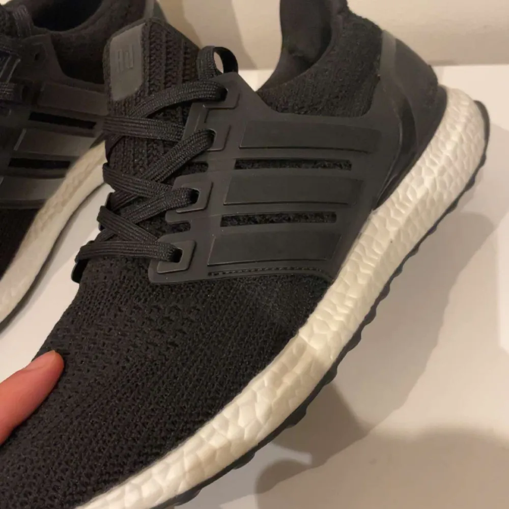 Säljer ett par svarta Adidas Ultraboost i mycket bra skick. De har en snygg och stilren design med stickat material och klassiska tre ränder på sidan. Perfekta för både träning och vardag. . Skor.