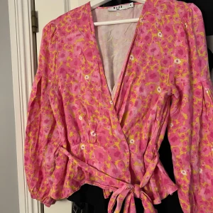 Knytblus - Säljer denna superfina knyt/wrap blusen från NA-KD. Storlek 38. Rosa med gult och vit blomliknande mönster. Säljer för 150kr + frakt eller prisförslag🩷