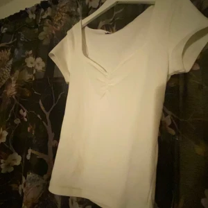 Vit kortärmad topp - Säljer en superfin vit topp med korta ärmar och en snygg v-ringad detalj framtill. Perfekt som ett basplagg i garderoben och är helt oanvänd 🌸 Toppen har en tight passform och är i storlek Xs men passar även som Xxs🤍 