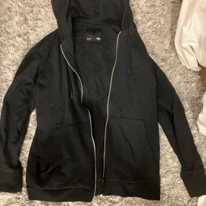 Svart munk tröja  - Säljer en svart munk tröja från lager 157 i storlek S. Den har en dragkedja framtill och en mysig huva. Perfekt för kyliga dagar eller som ett extra lager. Använd men i bra skick. 