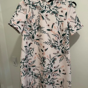 Blommig klänning med knytband - Säljer en superfin blommig klänning i ljusa färger med gröna och rosa detaljer. Den har korta ärmar och ett snyggt knytband i ryggen. Perfekt för vår och sommar! 🌸