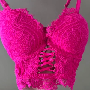Neonrosa spetskorsett - Säljer en superfin neonrosa korsett med spetsdetaljer och snörning framtill. Den har justerbara axelband och en vacker spetskant längst ner. Perfekt för en festlig kväll eller som en statement piece under en kavaj. Använd ett fåtal gånger, så den är i mycket bra skick!