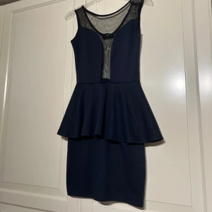 Mörkblå klänning från Club L - Snygg mörkblå klänning från Club L i strl S med transparent mesh upptill och en peplumdetalj i midjan. Perfekt för festliga tillfällen! Klänningenn har en tight passform som framhäver figuren. Materialet känns bekvämt och stretchigt. 