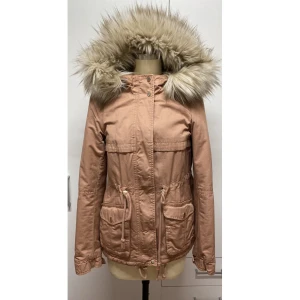 Rosa-Beige parkajacka med fuskpäls - Säljer en snygg rosa-beige parkajacka med fuskpäls på huvan. Jackan har långa ärmar och praktiska fickor framtill. Perfekt för höst och vinter, med dragkedja och knappar för extra värme. Den har en justerbar midja för bättre passform. Supermysig och stilren!