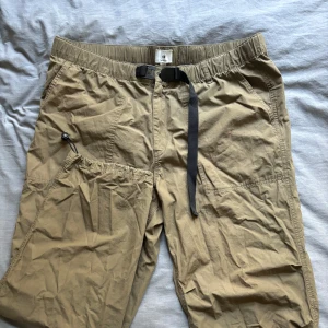 Beige Parschute Pants från H&M - Militär/olivgröna parachute byxor i bomull med spännband från H&M, med justerbar fotöppning Använda några få gånger, se bild för defekter Säljer då det ej är min stil längre (L: 105cm, W: 50cm, Innersöm: 75cm, Benöppning: 20cm