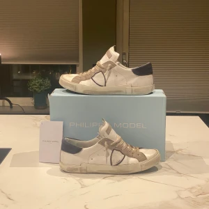 Philippe Models - Tja! Säljer nu ett par snygga vita sneakers från Philippe Model med mörkblå detaljer och beige snörning. Skorna har en stilren design med en mix av material som ger en unik look. Perfekta för en trendig vardagsstil men även fest 💙🍾Köpte dem i somras för 3000kr från Cettire. Allt OG medföljer! Hör av er vid frågor eller funderingar! 😁Kan vara intressant med byten!
