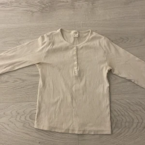 Vit ribbad tröja från Zara - Säljer en stilren vit ribbad tröja från Zara i storlek 10. Tröjan har långa ärmar och en knappdetalj framtill som ger en snygg touch. Perfekt för en avslappnad look.