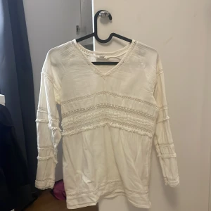 Vit topp med spetsdetaljer - Säljer en vit 3/4 långärmad topp med lite  v-ringning och vackra spetsdetaljer. Perfekt för en stilren och elegant look. Passar bra till mycket 