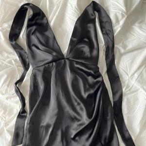 Svart klänning från Zara - Svart klänning från Zara i satin med djup v-ringning och öppen rygg. Oanvänd.