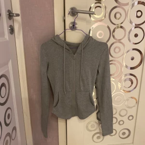 Grå yoga tröja med dragkedja - Säljer en  grå yoga kofta med dragkedja och huva. Tröjan har långa ärmar och praktiska fickor framtill. Perfekt för en avslappnad look. ger en smal midja, polyester, varm fodrad inne