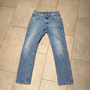 Levis 501 jeans i blå denim - Klassiska Levis 501 jeans i blå denim. Dessa jeans har en straight passform och är tillverkade i bomull. Perfekta för en avslappnad stil med sin ikoniska design och slitstarka material.