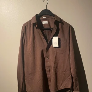 Brun skjorta från These Glory Days - Snygg brun skjorta från These Glory Days i regular fit. Skjortan har långa ärmar och knappar framtill. Perfekt för en stilren look. Aldrig andvänd. Storlek 37/38/S. MVH Filip 