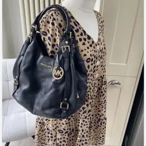 Äkta Michael Kors väska med gulddetaljer och logotyp. Väskan har dubbla handtag och justerbara spännen på sidorna. Perfekt för att bära med sig det viktigaste med stil.