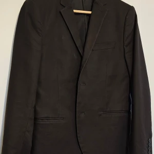 Kavaj - Elegant svart kavaj med klassisk design och knappar framtill. Perfekt för formella tillfällen och stiliga outfits.