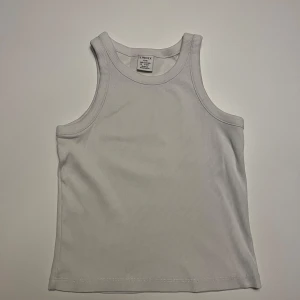 Vit ribbad linnetopp från Lindex - Säljer en vit ribbad linnetopp från Lindex för barn. Perfekt för varma sommardagar eller som ett basplagg i garderoben. Enkel och stilren design.