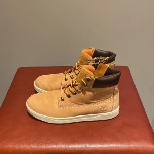 Bruna boots från Timberland - Snygga bruna boots från Timberland med snörning och vadderad krage i mörkbrunt. Perfekta för höst och vinter med en robust design och bekväm passform.