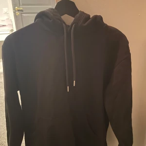 Svart hoodie - Säljer en klassisk svart hoodie med justerbar dragsko i huvan. Perfekt för en avslappnad stil och passar till det mesta. Den har en stor ficka framtill för extra bekvämlighet.