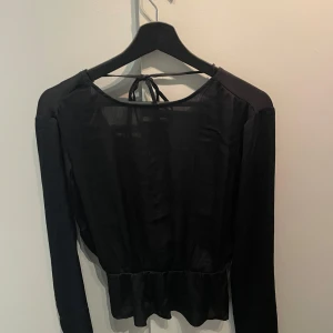 Svart långärmad topp med öppen rygg - Snygg svart långärmad topp med öppen rygg och knytning i nacken. Perfekt för en stilren och elegant look. Tillverkad i ett lätt och luftigt material.