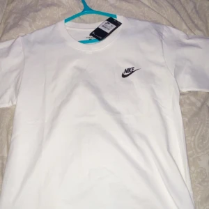 Vit t-shirt från Nike - Säljer en klassisk vit t-shirt från Nike med logga på bröstet. Perfekt för en avslappnad stil. T-shirten är kortärmad och gjord i bomull för en bekväm passform.
