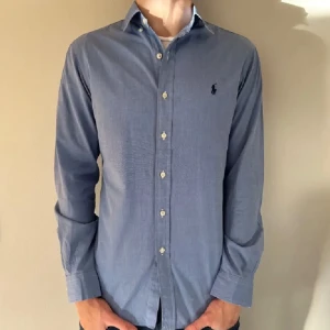 Blå skjorta från Ralph Lauren - Snygg blå skjorta från Ralph Lauren i slim fit. Tillverkad i 100% bomull med stretch för extra komfort. Skjortan har långa ärmar och klassiska knappar framtill. Perfekt för en stilren look. Säljer den då den är för liten för mig, därav så säljer jag den, den är i bra skick. Pris 325 snabb affär 300kr