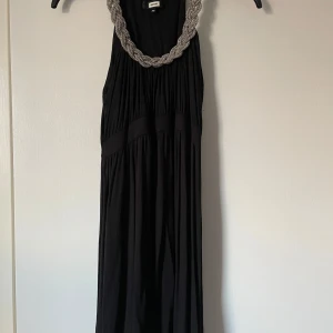 Svart klänning från BikBok - Elegant svart långklänning från Bik Bok med en vacker pärldetalj runt halsringningen. Klänningen har en flytande passform och är perfekt för speciella tillfällen.
