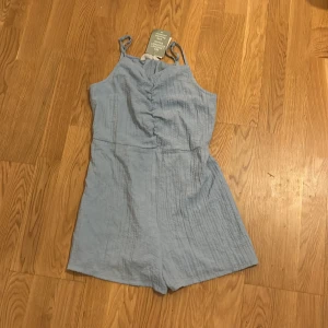 Ljusblå jumpsuit från H&M Oanvänd  - Snygg ljusblå jumpsuit från H&M med smala axelband och elastisk midja. Perfekt för varma sommardagar. Tillverkad i ett lätt och luftigt material som ger en avslappnad look. Oanvänd 