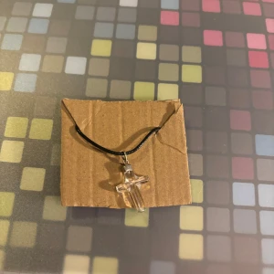 Halsband med genomskinligt kors - Snyggt halsband med ett genomskinligt kors som hänge. Korset är fäst på en svart rem, vilket ger en stilren och enkel look. Perfekt för att komplettera din outfit med en subtil detalj.