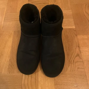 Svarta boots från UGG - Säljer ett par svarta UGG boots i mjukt material med varm insida. Perfekta för kyliga dagar och ger en stilren look. De har en klassisk design med rund tå och är lätta att matcha med olika outfits. Kan räkna på fingrarna hur många gånger dom är använda då jag tyvärr kände att dom inte passa mig.