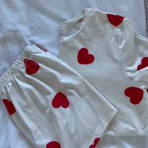 Vit pyjamas med röda hjärtan - Mysig vit pyjamas med kortärmad topp och shorts, dekorerad med röda hjärtan. Perfekt för en bekväm natt.