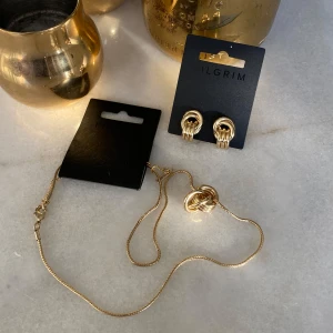 Pilgrim Guldörhängen Och Halsband - Snyggt set med guldörhängen och matchande halsband från Pilgrim. Örhängena har en elegant design med flera ringar, och halsbandet har en liknande knutdetalj. Nypris ligger på 500 kr sammanlagt, aldrig använda 💗