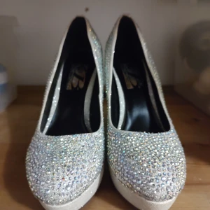Glittriga pumps med klack - Snygga glittriga pumps med hög klack och rund tå. Perfekta för en festlig kväll eller speciella tillfällen. Skorna har en elegant design med en glittrande yta som fångar ljuset.
