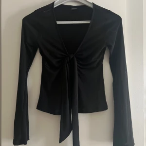 Svart långärmad topp med knyt - Snygg svart långärmad topp från gina tricot med knyt framtill. Toppen har en djup v-ringning och vida armar.